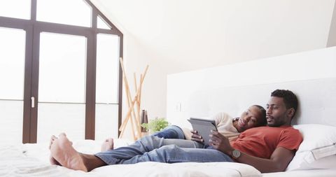 Couple Relaxing on Bed Together with Tablet in Bright Room