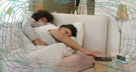 Intimate morning cuddle spooning couple reaching for smartphone on bedside nightstand