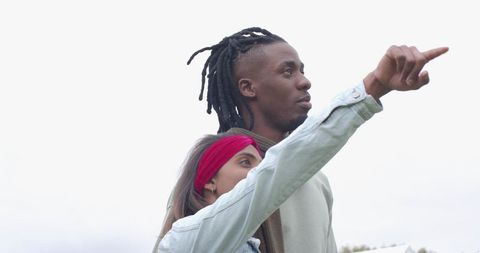 Diverse couple pointing toward horizon in overcast field, outdoor lifestyle moment