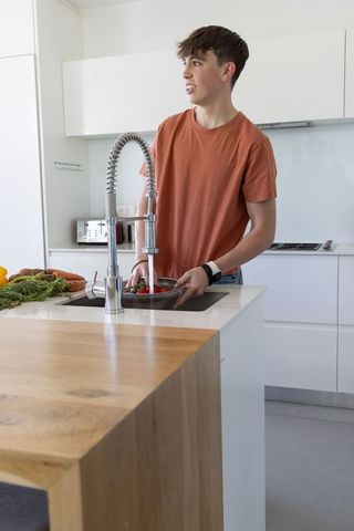 Teen rinsing vegetables at modern kitchen island with coil-spring faucet, minimalist style