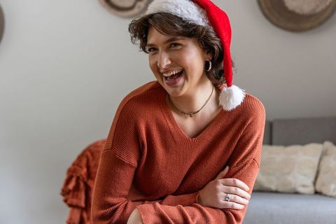 Laughing young woman wearing santa hat on cozy couch warm holiday lifestyle portrait