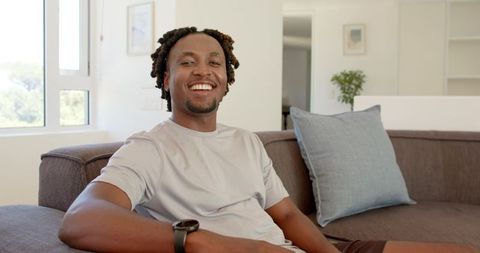 Smiling african american man relaxing on modern sofa in bright minimalist living room