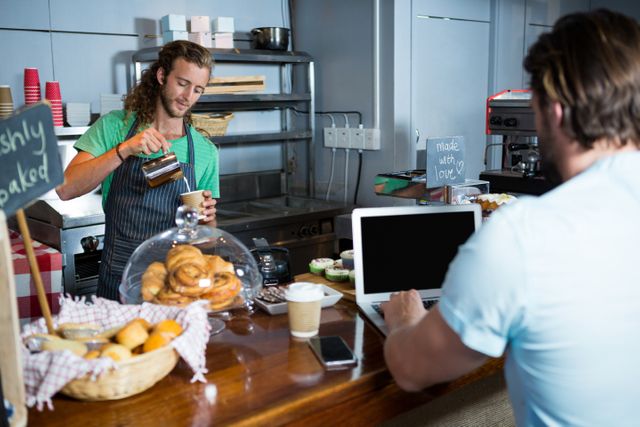 Customer using laptop at counter while staff preparing coffee in coffee shop