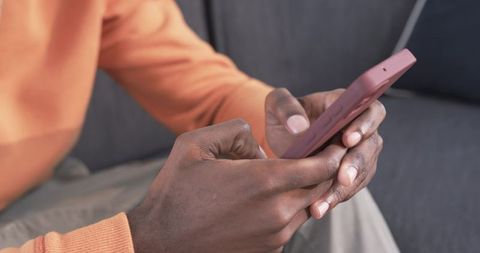 African American male holding mauve smartphone tapping screen on gray sofa lifestyle
