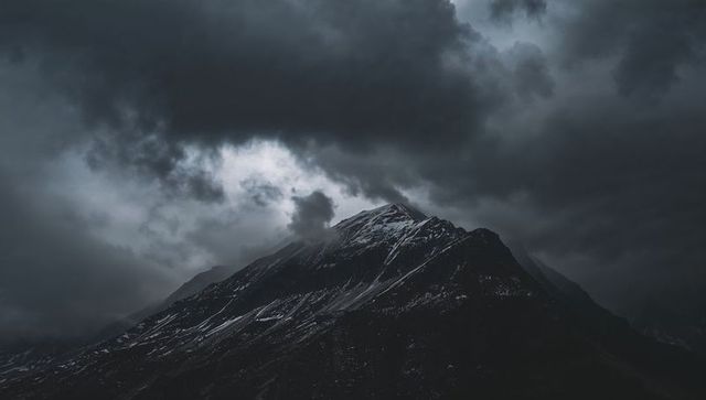 Looming snow-capped alpine peak under dramatic storm clouds and moody light