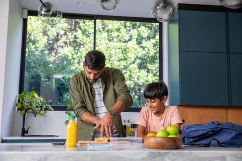 Father slicing bread with son observing in modern kitchen