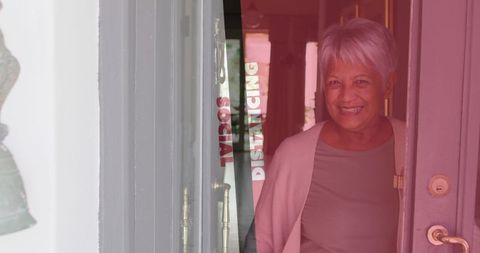 Senior woman smiling at doorway emphasizing social distancing