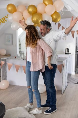 Couple celebrating at home under peach white gold balloons with bunting and casual style