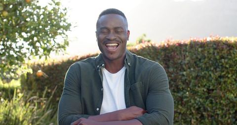 Laughing african american man enjoying sunny backyard with orange tree, casual green shirt