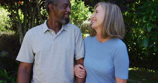 Diverse senior couple walking in their garden arm in arm in the sun smiling - Download Free Stock Photos Pikwizard.com