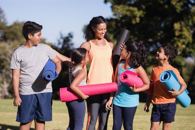 Happy children with female instructor holding exercise mats at park