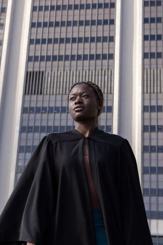 African american graduate standing confident in black gown before modern campus building