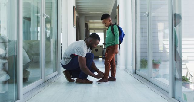 African american father helping his son with tying shoes in hallway. staying at home in self isolation during quarantine lockdown.