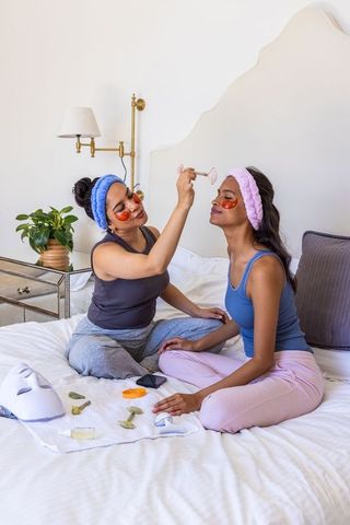 Diverse friends enjoying home spa night using rose quartz roller and under-eye gel patches