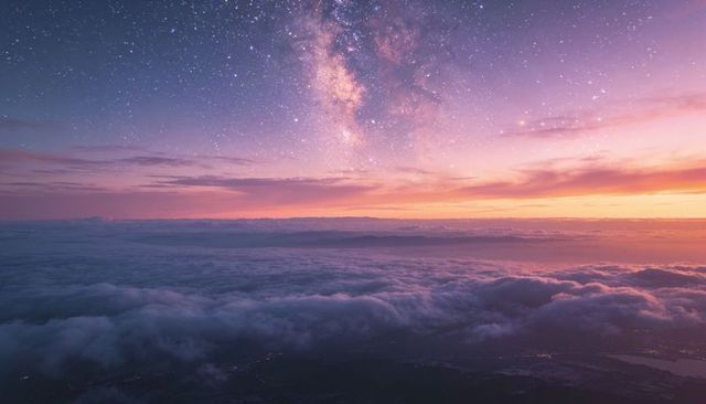 Milky way emerging over layered dawn cloudscape from high ridge with faint city glow