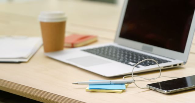 A well-organized office desk features a laptop, smartphone, and coffee cup. Essential tools for productivity are neatly arranged, signaling a professional work environment.
