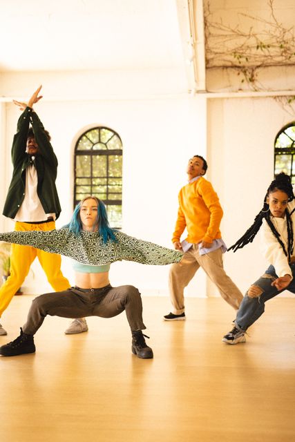 Diverse group of young adults performing a dance routine in a bright, spacious studio. Ideal for use in articles or advertisements related to dance, fitness, teamwork, creativity, and lifestyle. Perfect for promoting dance classes, workshops, or community events.