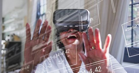 Senior woman exploring virtual reality using headset and reaching toward transparent digital interfa