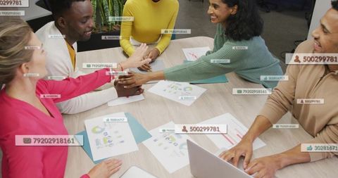 Team joining hands over meeting table with charts, laptop and analytics overlays