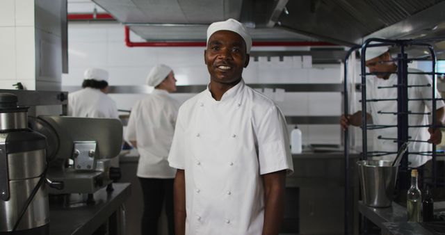 Close-up of a smiling Afro American chef in a professional kitchen. Ideal for advertisements, culinary articles, restaurant promotions, and content focused on teamwork in cooking environments.