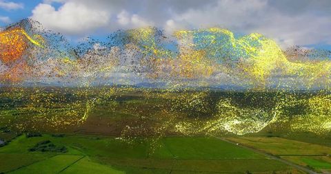 Drifting luminous particle ribbon above aerial farmland with golden ethereal glow