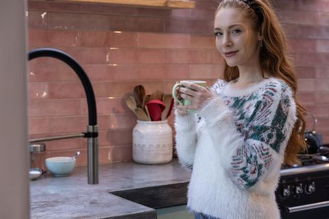 Red-haired woman sipping hot drink in cozy modern kitchen
