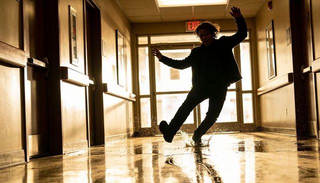 Backlit silhouette slipping through wet hallway creating dramatic splash and reflections