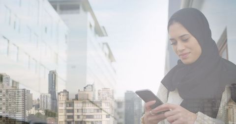 Smiling Woman in Hijab Using Smartphone Against Urban Backdrop