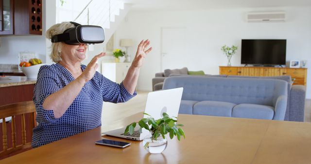 A senior woman is using a VR headset at home, engaging with modern technology. Ideal for use in articles or advertisements about technology for seniors, innovation in virtual reality, tech adoption among older adults, or product promotions for VR devices.