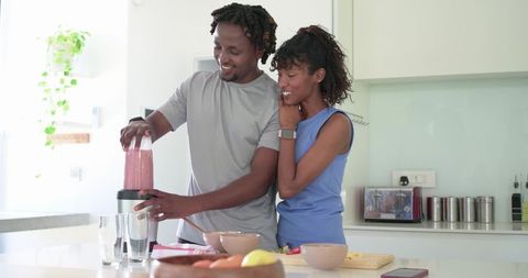 African couple preparing healthy smoothie together in bright modern kitchen
