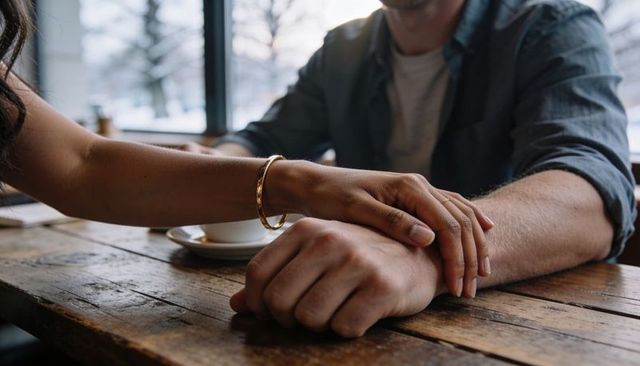 Couple sharing warm moment in cozy cafe holding hands over wooden table with gold bangle