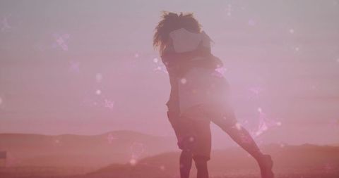 Backlit couple embracing at golden sunset with butterfly bokeh, intimate desert silhouette