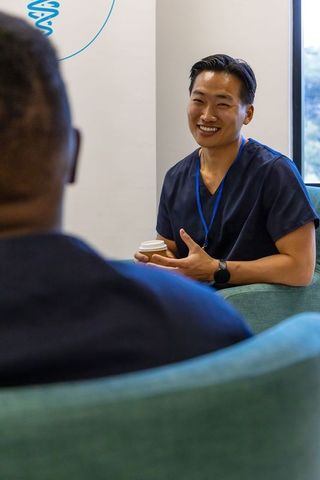 Smiling healthcare worker chatting with colleague in clinic lounge holding coffee, modern clinic