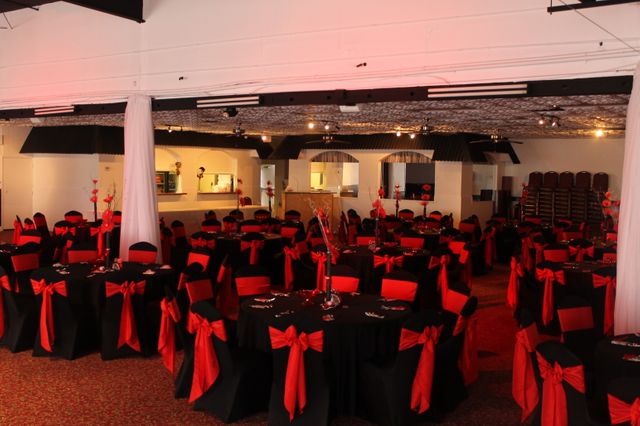 Image showcases an elegant banquet hall setup adorned with black tablecloths and red chair covers. Ideal for special events like weddings, corporate gatherings, and formal dinners. Vivid colors and elegant decor create a sophisticated atmosphere perfect for marketing event venues or party services.