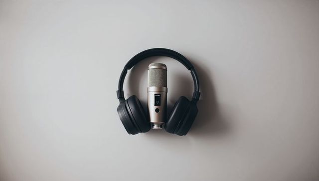 Minimalist condenser microphone wearing over-ear headphones on studio tabletop