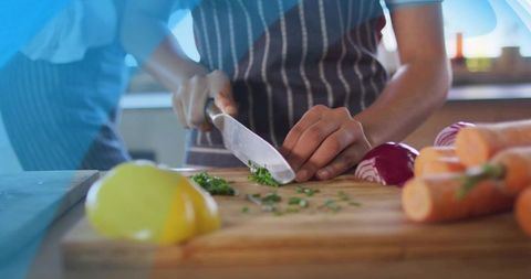Close-up woman chopping herbs and vegetables on wooden cutting board with chef knife