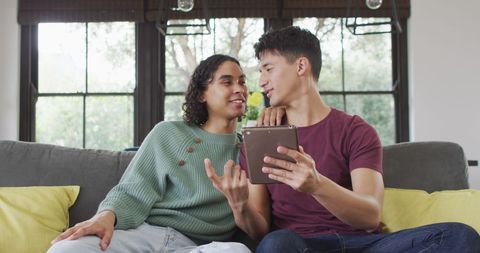 Diverse Male Couple Relaxing and Using Tablet Together Indoors