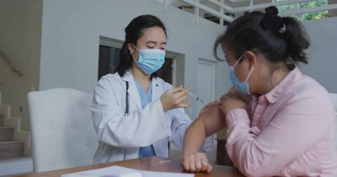 Clinician administering vaccine to adult patient wearing mask during indoor clinic consultation