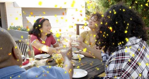 Sunlit backyard toasting friends celebrating alfresco gathering with wine and confetti