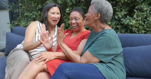 Mature diverse women sharing laughter and high five on outdoor patio sofa