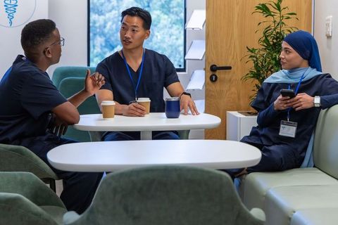 Healthcare team taking coffee break in clinic lounge, multicultural nurses chatting
