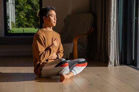 Asian man practicing breathwork and mindfulness in sunlit home interior
