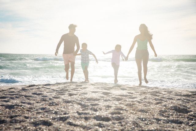 Family enjoying a sunny day at the beach, running and holding hands. Perfect for promoting family vacations, summer activities, and lifestyle content. Ideal for travel brochures, family-oriented advertisements, and social media posts about family bonding and outdoor fun.