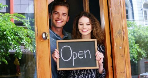 Cheerful couple opening cafe with welcome sign
