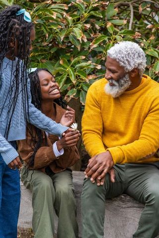 African american grandfather sharing smile with granddaughters holding daisy outdoors