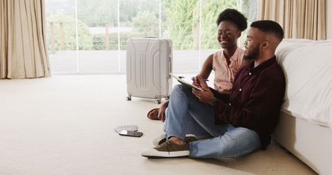 Couple planning vacation with tablet at home next to suitcase