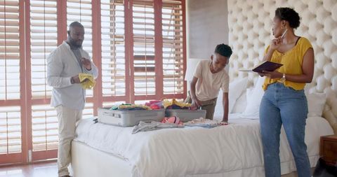 African American Family Packing Suitcases on King Bed While Parents Planning Trip on Tablet