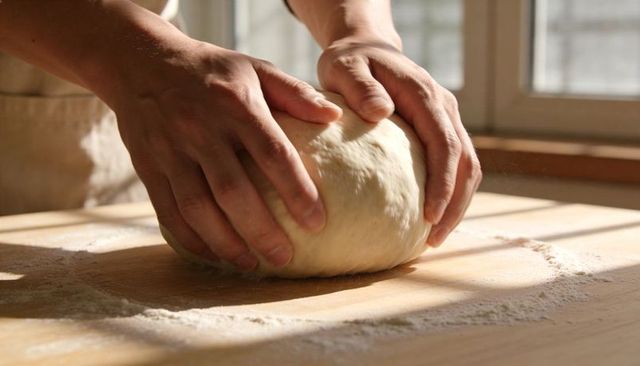 Artisan Hands Kneading Dough on Sunlit Wooden Board for Homemade Bread