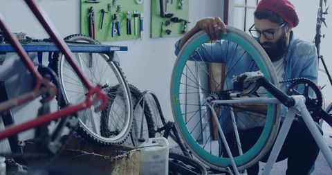 Bicycle mechanic repairs teal rimmed wheel in busy workshop