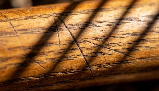 Sunlit weathered wood railing macro revealing grain, scratches, patina and diagonal shadows
